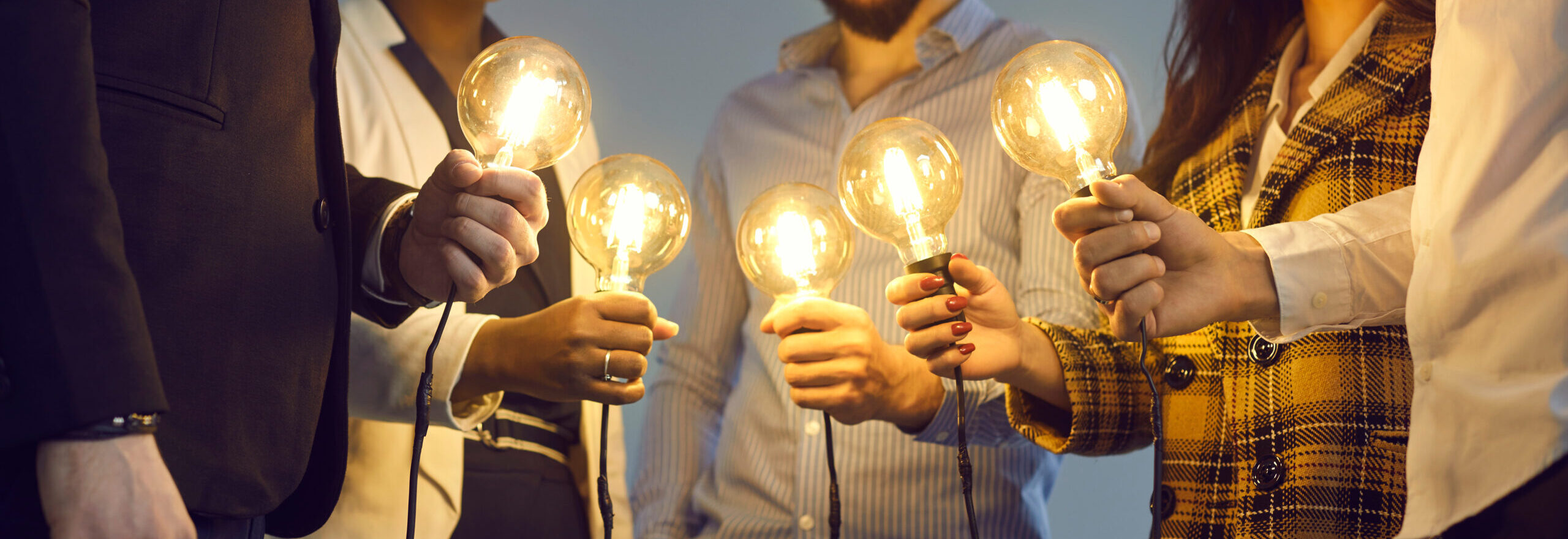Group of happy young multiethnic people holding glowing lit retro Edison lightbulbs. Multiracial business team joining shining electric light bulbs as metaphor for teamwork and sharing creative ideas